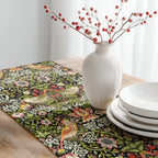 Decorative table setting with William Morris table runner featuring Strawberry Thief pattern with black base, white vase with branches, and white plates.
