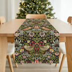 William Morris Strawberry Thief table runner with floral and bird pattern on a wooden table in front of a Christmas tree.