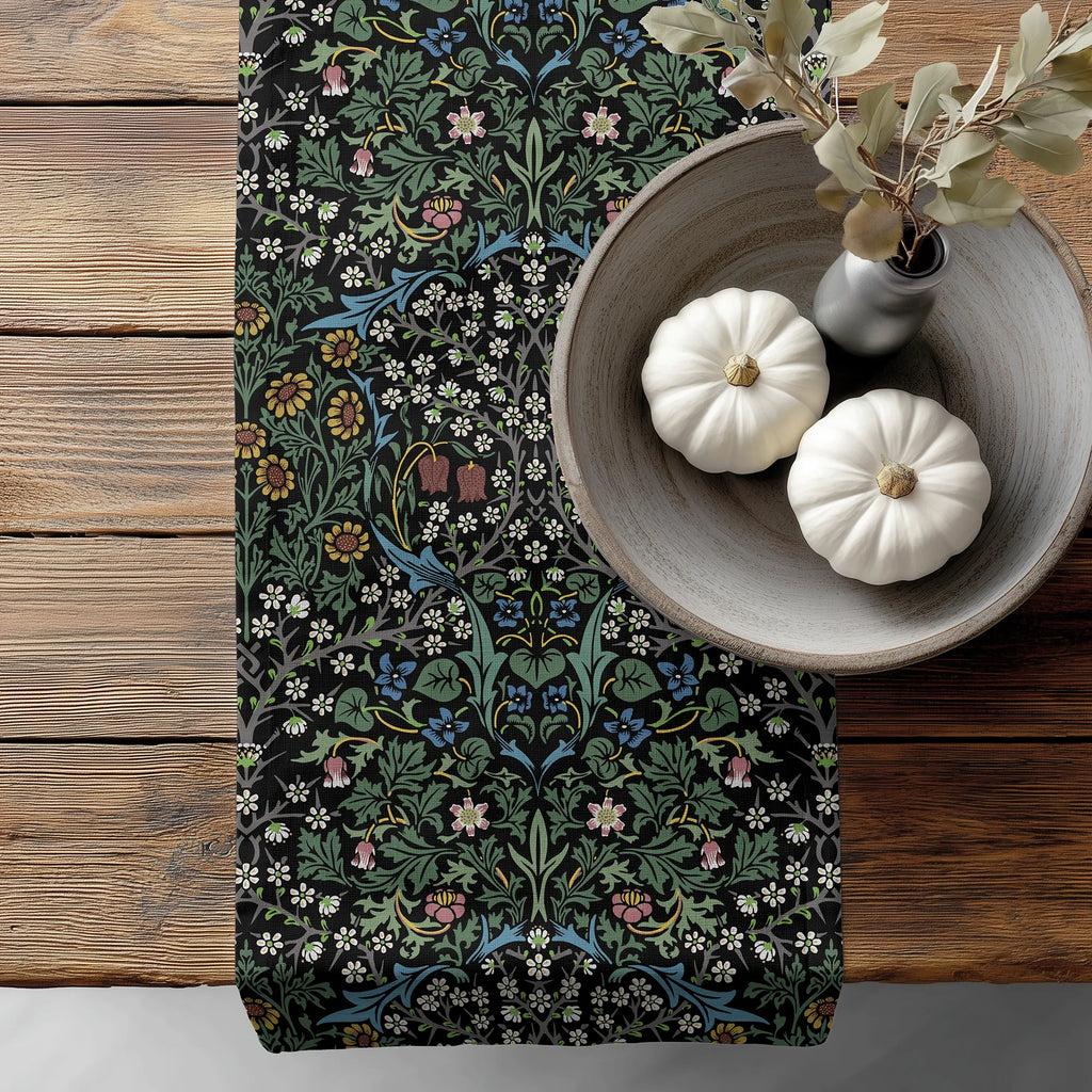 William Morris Blackthorn table runner in Classic Black, with floral pattern, on a wooden surface with pumpkins and a vase.