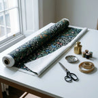 A roll of William Morris Blackthorn fabric in Classic Black part-unrolled on a work table with scissors and thread.