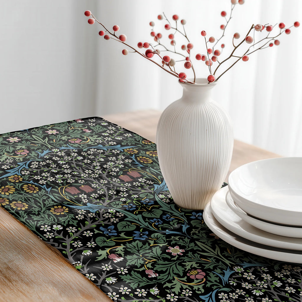 Decorative table setting with a William Morris table runner in classic black, white vase with red berries, and white plates on a wooden table.