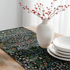 Decorative table setting with a William Morris table runner in classic black, white vase with red berries, and white plates on a wooden table.
