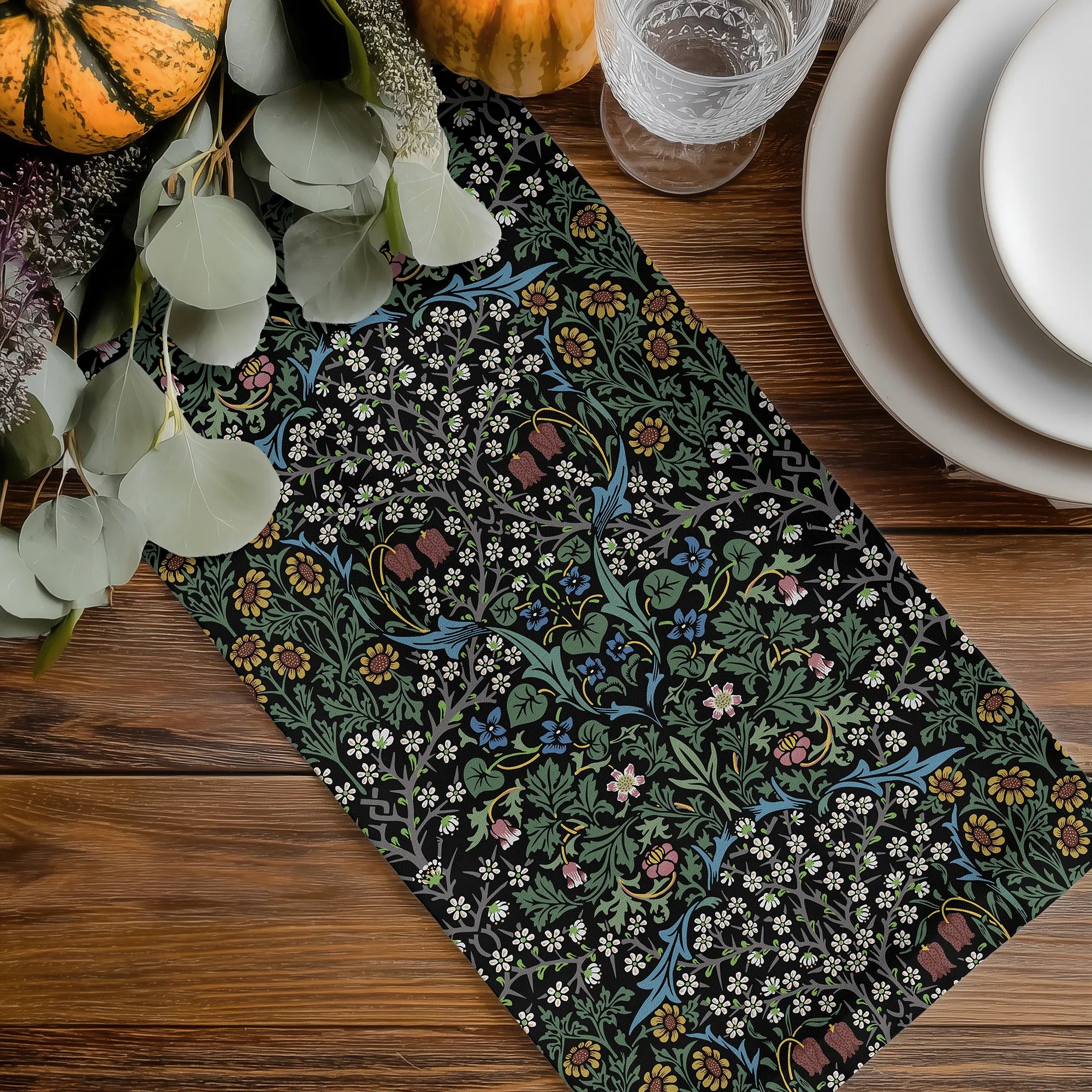 Decorative Halloween table runner with William Morris Blackthorn floral pattern on a wooden table with pumpkins and glasses.