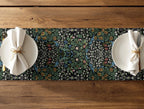 Two plates with folded napkins on a floral William Morris table runner over a wooden table.