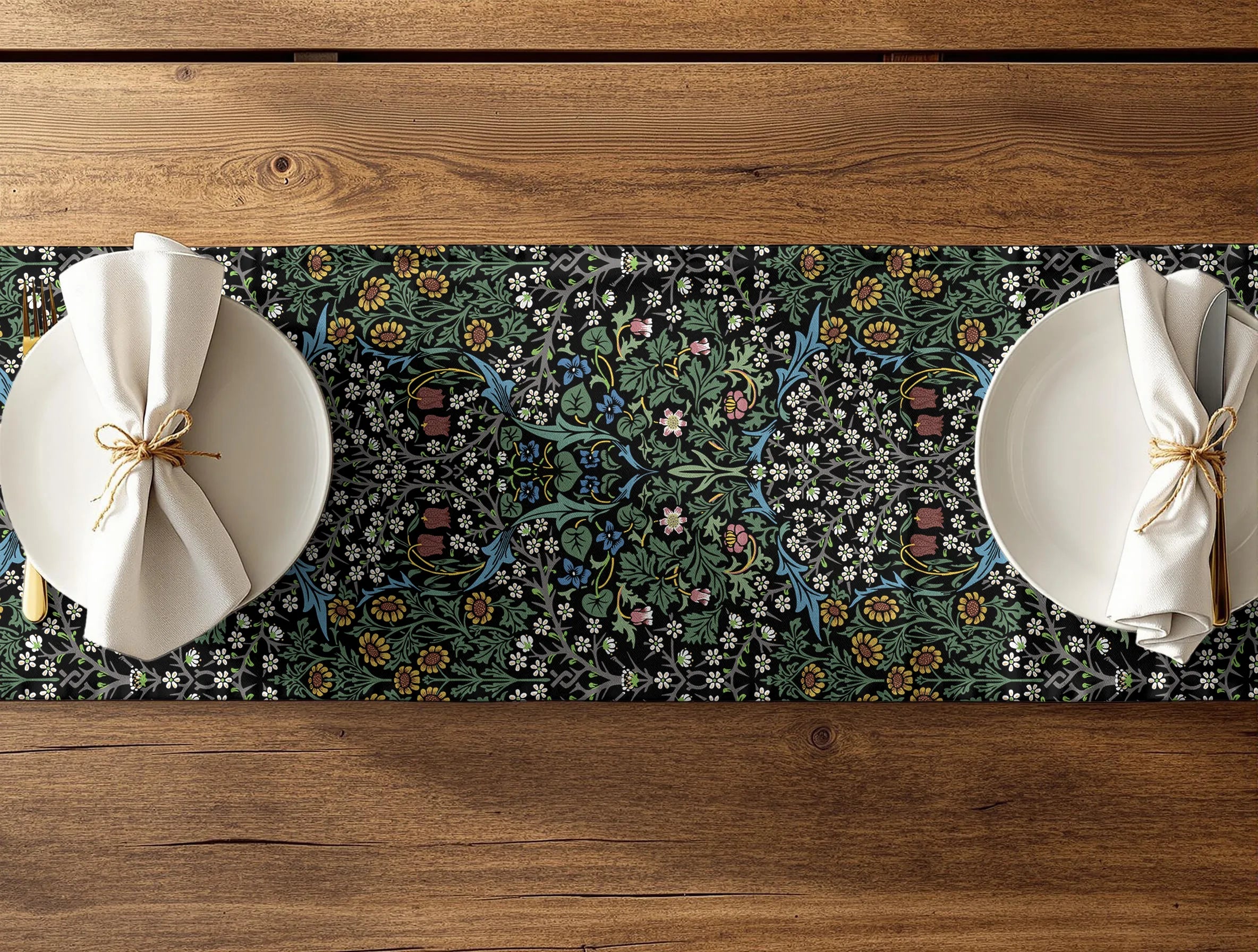 Two plates with folded napkins on a floral William Morris table runner over a wooden table.