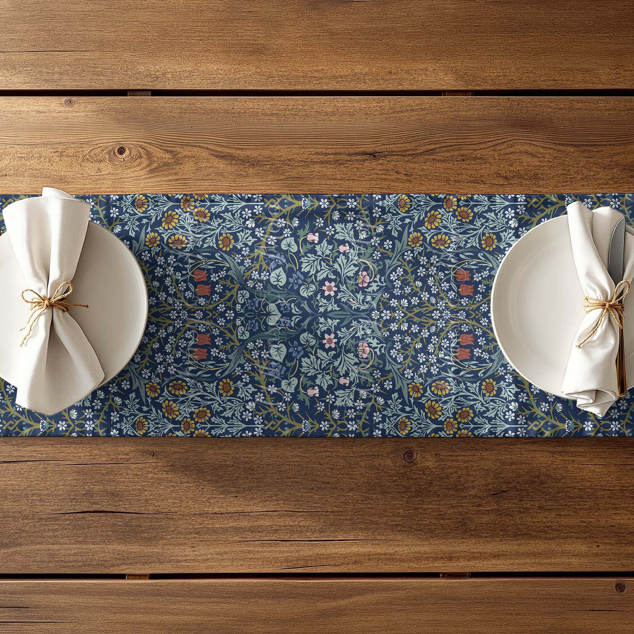 Blue floral William Morris table runner on a wooden table with white plates and napkins.