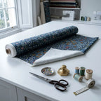 A roll of William Morris Blackthorn fabric in Dusky Blue Garden part-unrolled on a work table with scissors and thread.