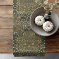William Morris Blackthorn table runner in Sultry Olive green, with floral pattern on a wooden surface with pumpkins and a vase.