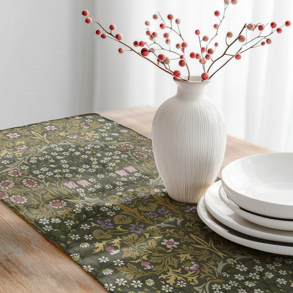 Decorative table setting with a William Morris table runner in olive green, white vase with red berries, and white plates.