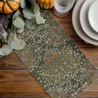 William Morris olive green table runner with floral pattern on a wooden table with pumpkins and glasses.