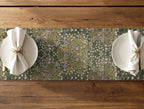 Floral patterned table runner - William Morris Blackthorn in olive green - with white plates and napkins on a wooden table.