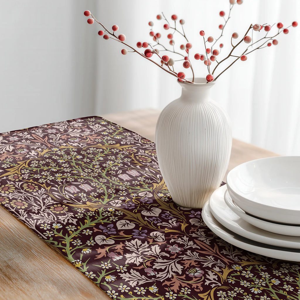 Table setting with a floral-patterned William Morris table runner in Maroon burgundy, white vase with red berries, and white plates.