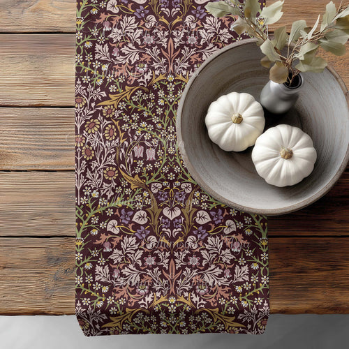 William Morris Blackthorn table runner in maroon and mauve, with floral pattern on a wooden surface with pumpkins and a vase.