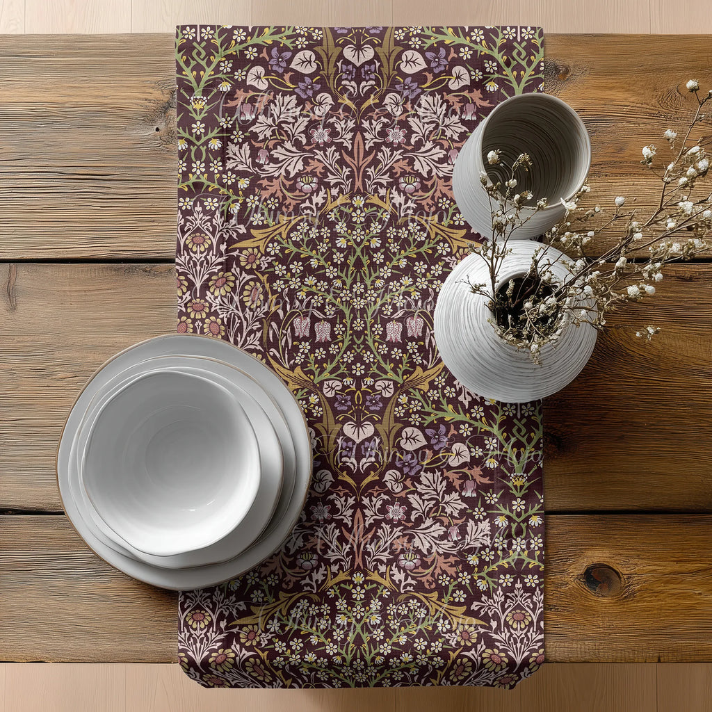 Table setting with floral-patterned William Morris table runner in maroon, white plates, and decorative vase on wooden table.