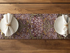 Two plates with napkins on a floral William Morris Blackthorn table runner over a wooden table.