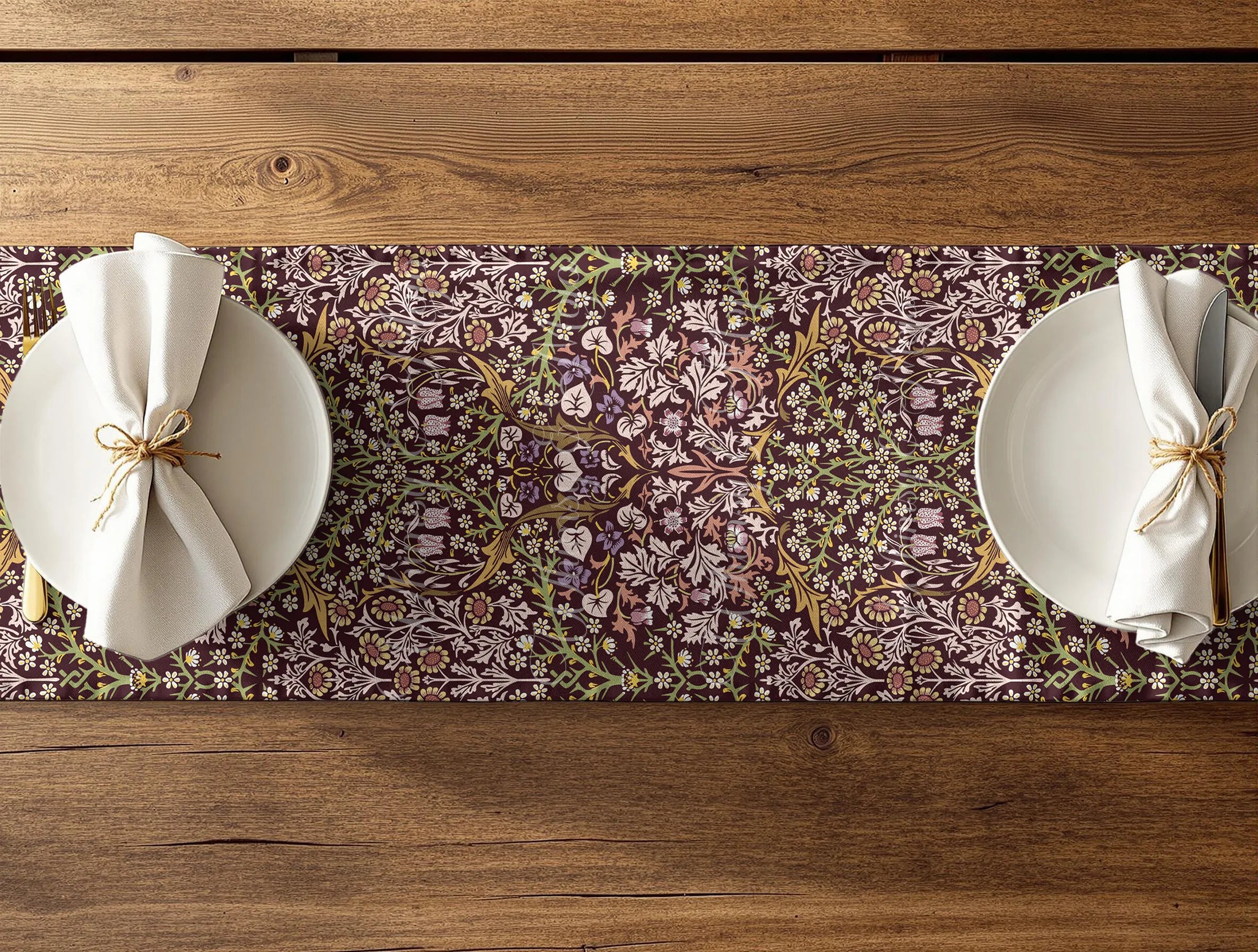 Two plates with napkins on a floral William Morris Blackthorn table runner over a wooden table.