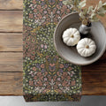 William Morris Blackthorn table runner in Earthy Garden, with floral pattern, on a wooden surface with pumpkins and a vase.