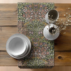Easter floral-patterned William Morris table runner in earth tones, on a wooden table with white plates and a vase.