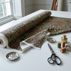 A roll of William Morris Blackthorn fabric in Secret Garden part-unrolled on a work table with scissors and thread.