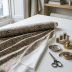 Blackthorn Heritage Taupe home decor fabric unrolled on a maker's cutting table with brass shears and thread spools