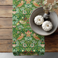 William Morris Strawberry Thief table runner styled on a wooden dining table with bowl centerpiece, showcasing the historic Arts and Crafts botanical pattern.