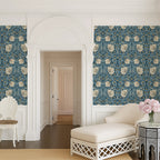Living room with decorative William Morris wallpaper in blue tones, white chair, and floral arrangement.