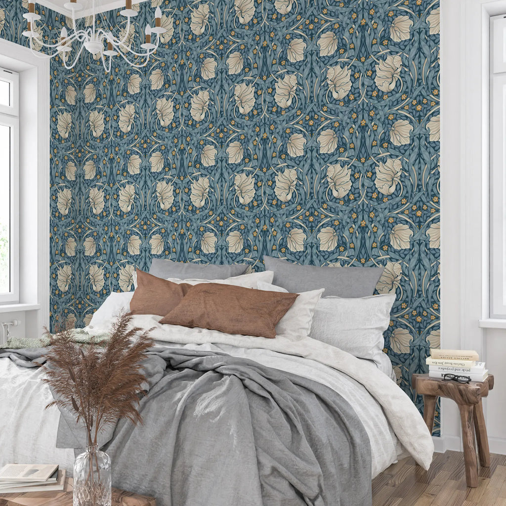 Bedroom with William Morris Pimpernel floral wallpaper, bed with pillows, and wooden side table.