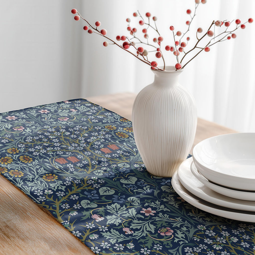Decorative table setting with a William Morris table runner in Blue floral pattern, white vase with red berries, and white plates.