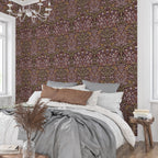 William Morris Blackthorn wallpaper in maroon featured behind a bed in a cozy bedroom, creating a warm heritage revival atmosphere with intricate floral pattern.