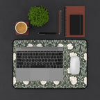 Laptop on a decorative William Morris mouse pad with a cup, plant, and stationery items on a dark surface