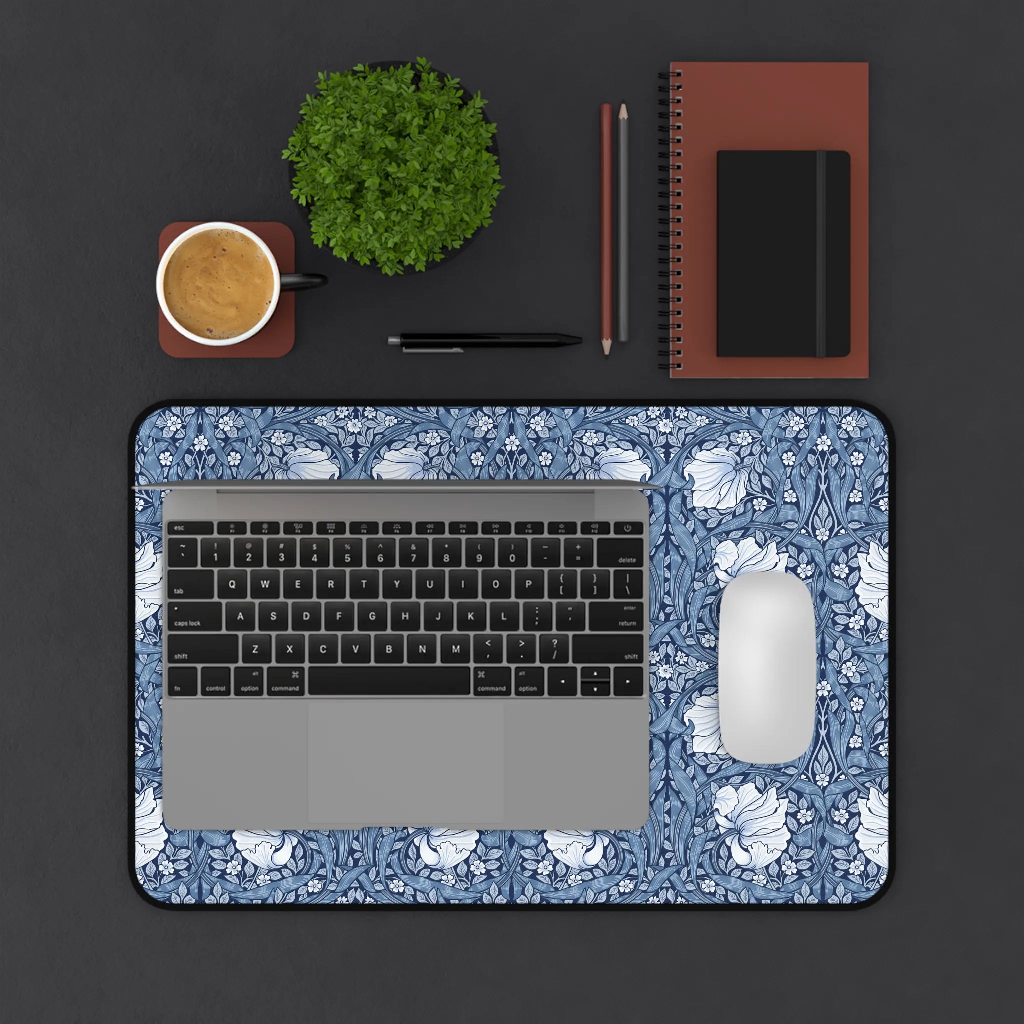 Laptop with floral William Morris desk mat mousepad on a dark surface with office items.