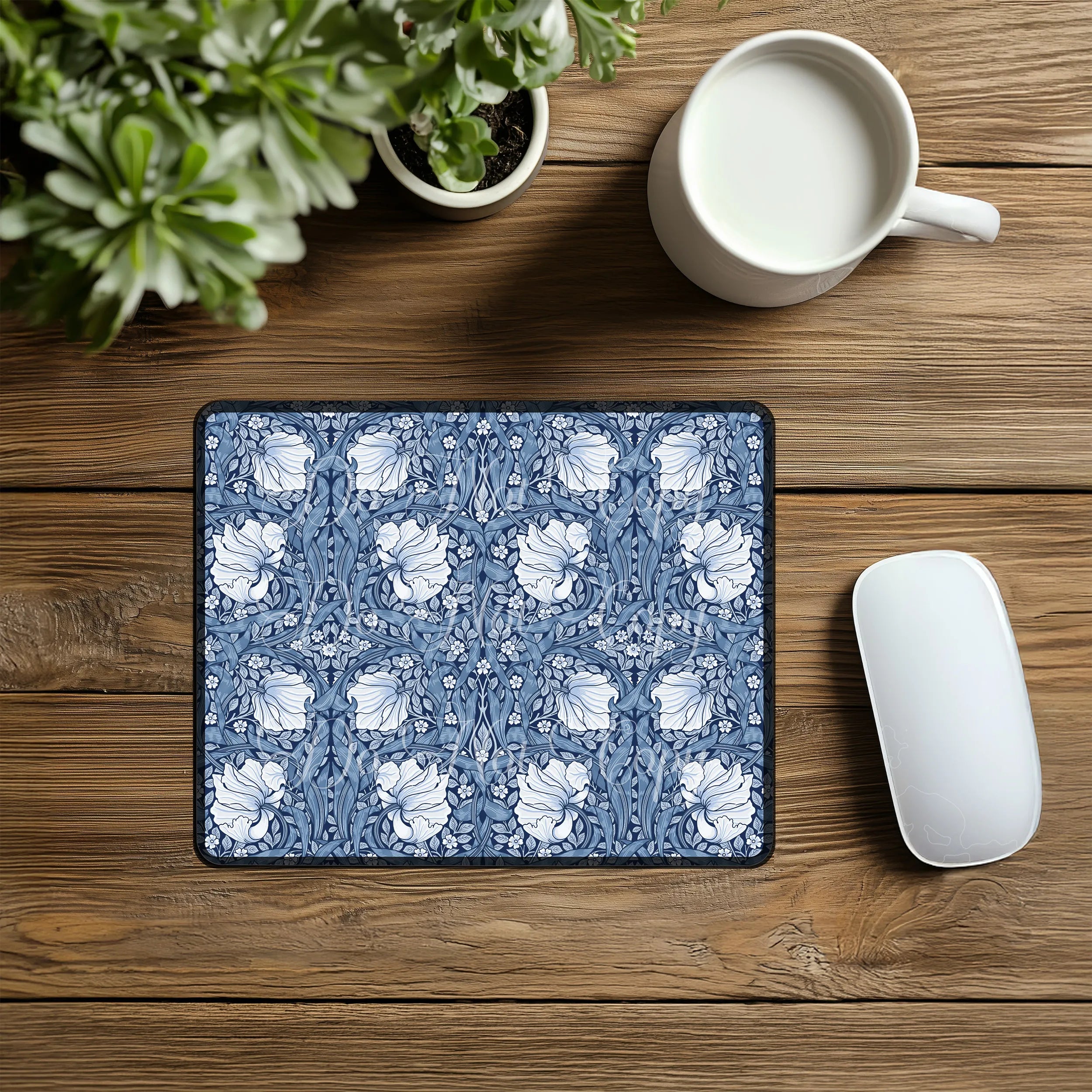 Floral patterned William Morris mouse pad on a wooden desk with a mug and plant. It features the blue Pimpernel pattern