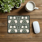 Decorative William Morris Pimpernel mouse pad with floral pattern in sage green and cream, on a wooden desk with a mug and plant.
