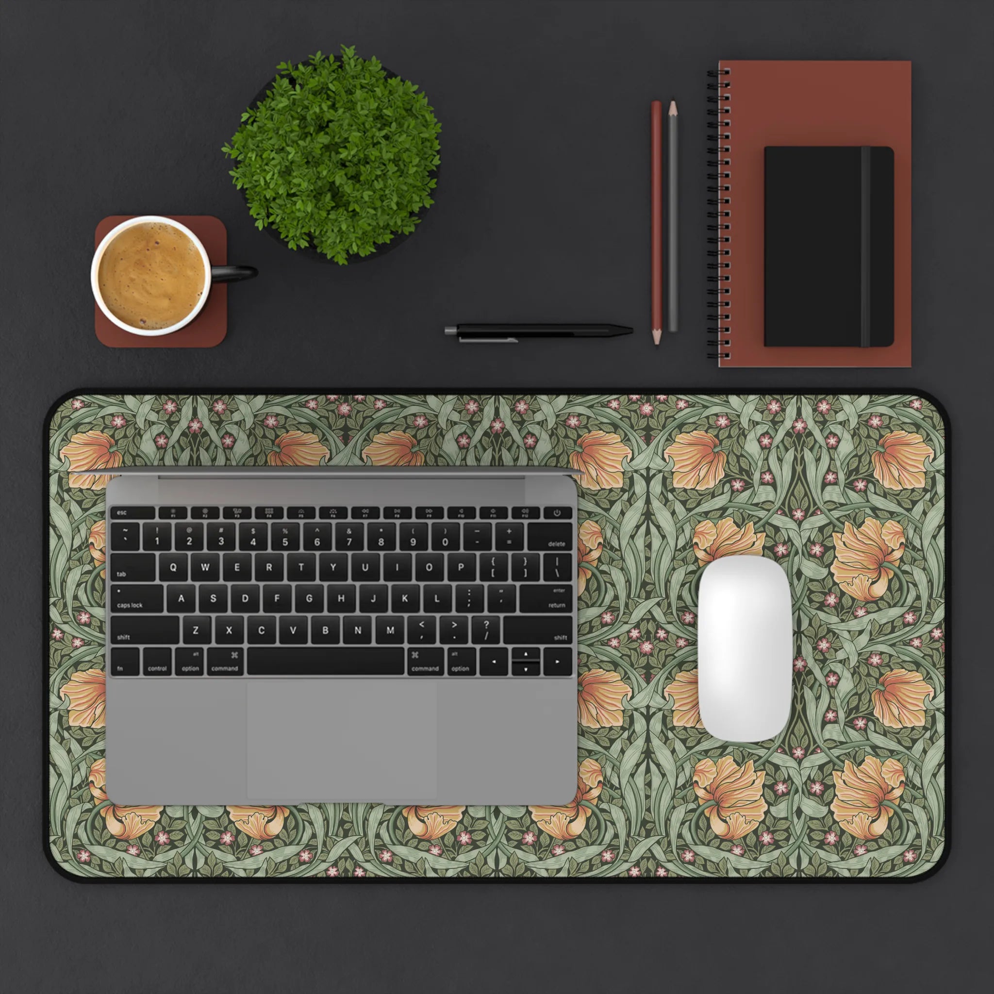 A laptop computer is on top of a William Morris Pimpernel desk mat featuring the iconic Pimpernel pattern in sage green and copper