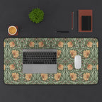A laptop computer is on top of a large William Morris desk mat featuring the iconic Pimpernel pattern in sage green and copper