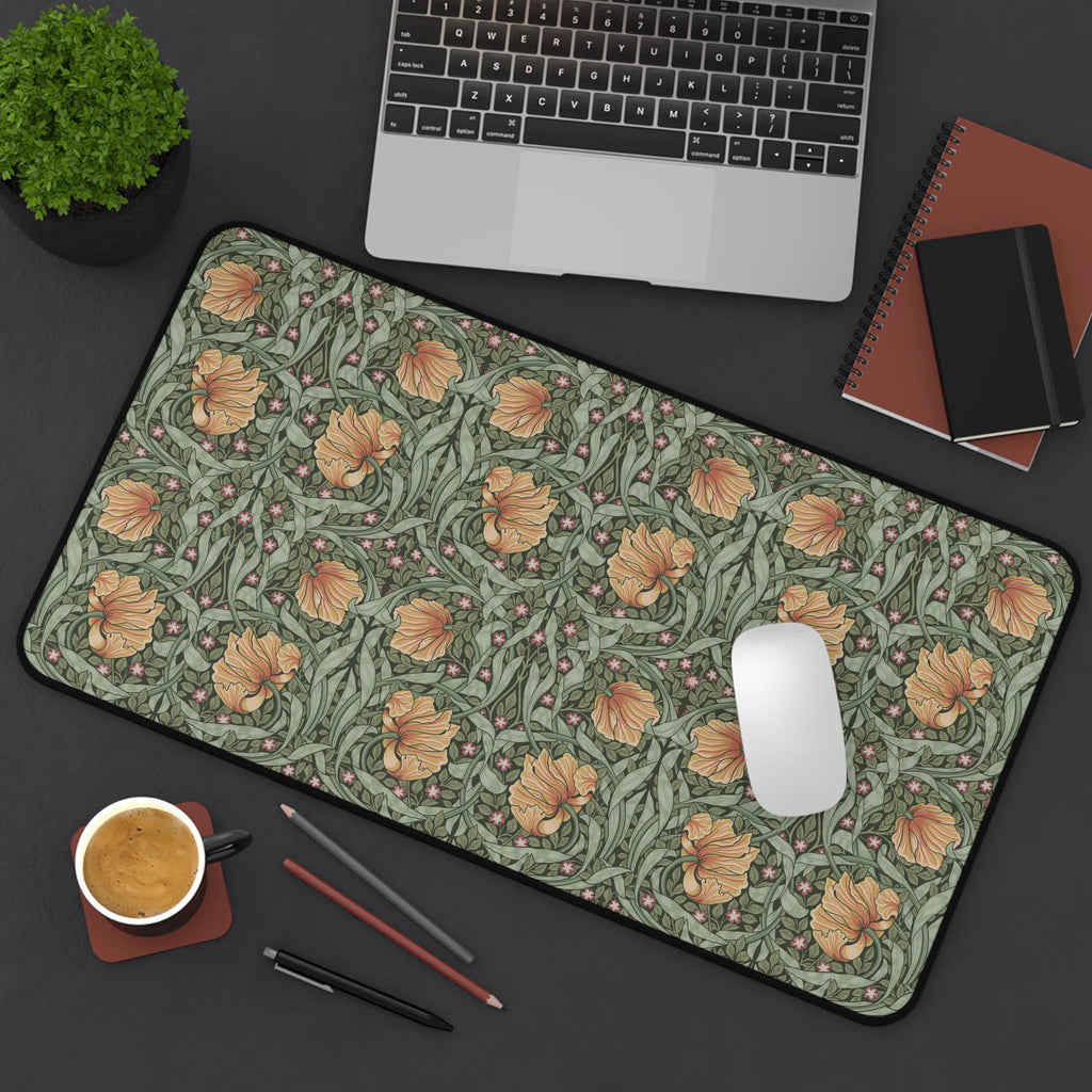 A flatlay scene of a William Morris desk mat featuring the iconic Pimpernel pattern in sage green and copper, with a laptop computer, a cup of coffee, notebooks and a plant