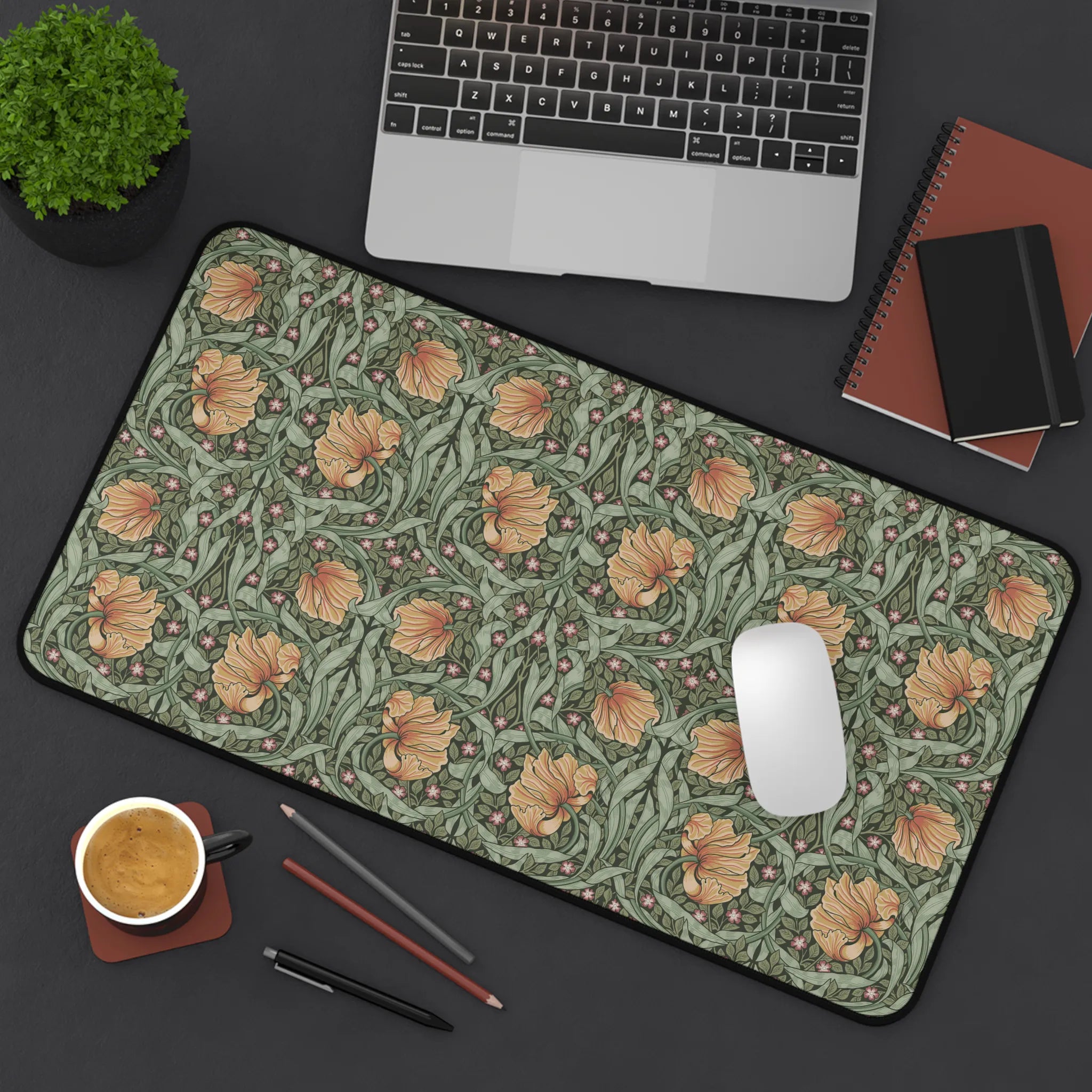 A flatlay scene of a William Morris desk mat featuring the iconic Pimpernel pattern in sage green and copper, with a laptop computer, a cup of coffee, notebooks and a plant