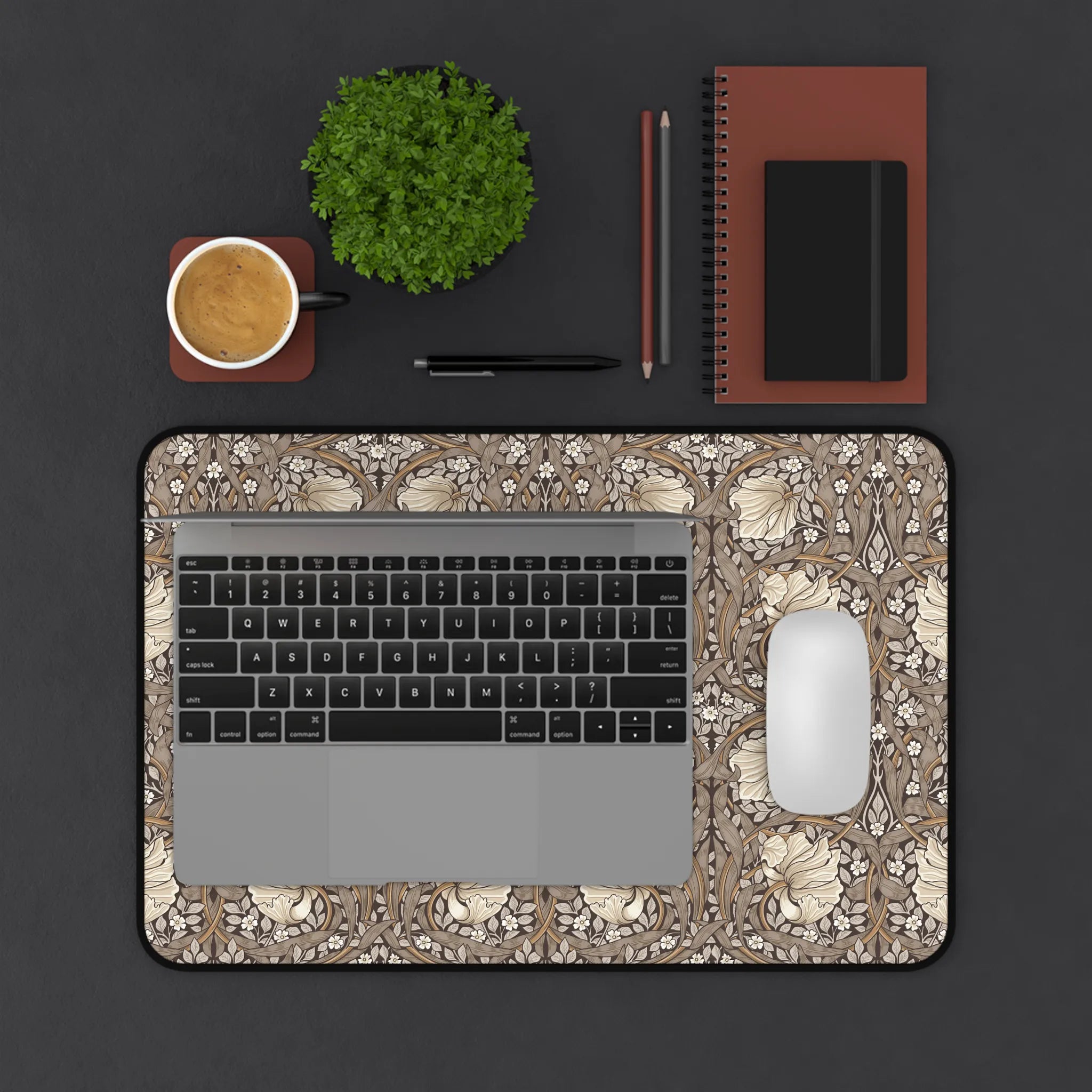 Laptop on a William Morris Pimpernel desk mat with a cup, plant, and office supplies on a dark surface