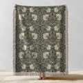 William Morris Pimpernel woven blanket displayed full length with fringe, botanical Arts and Crafts design in sage green and cream on ebony black