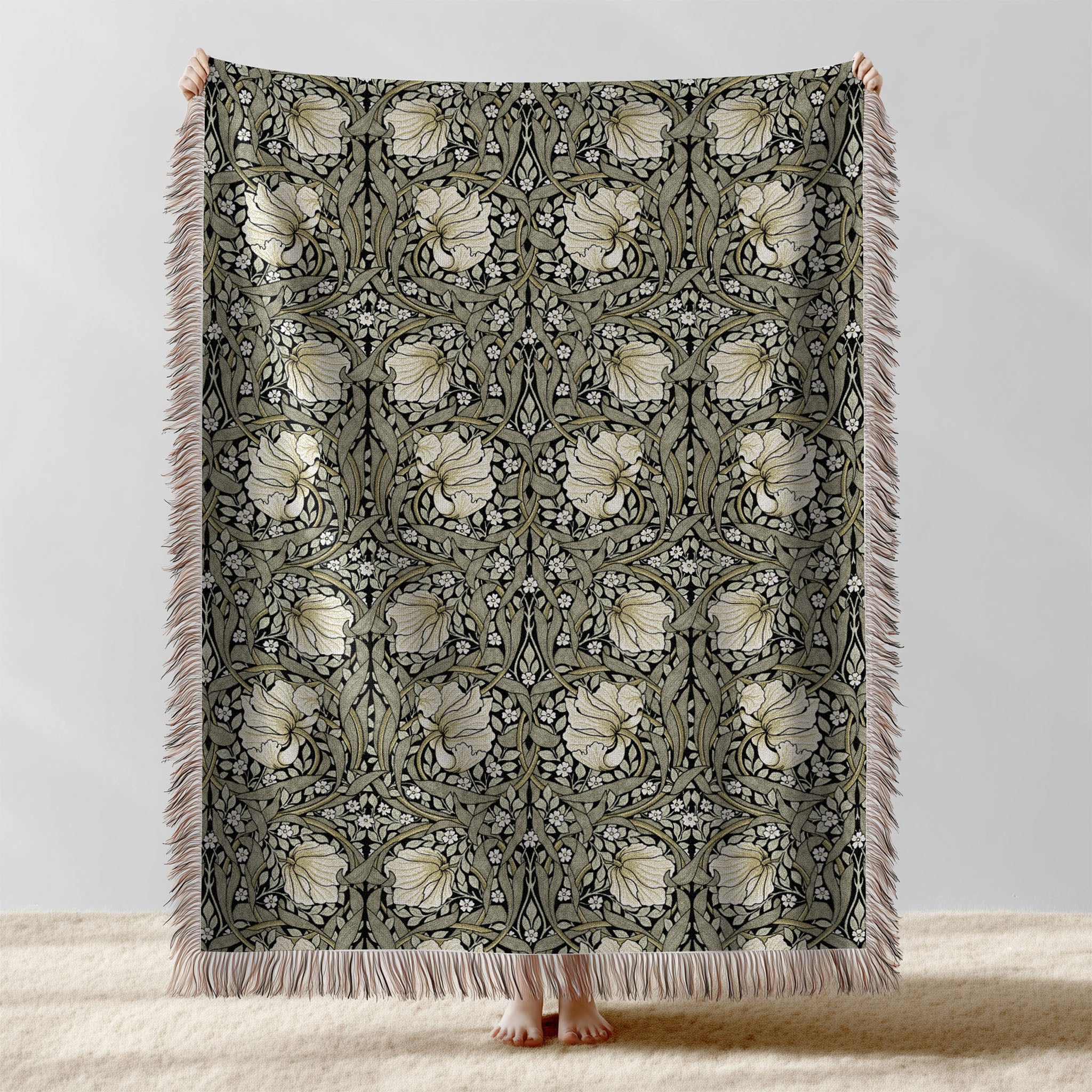 William Morris Pimpernel woven blanket displayed full length with fringe, botanical Arts and Crafts design in sage green and cream on ebony black