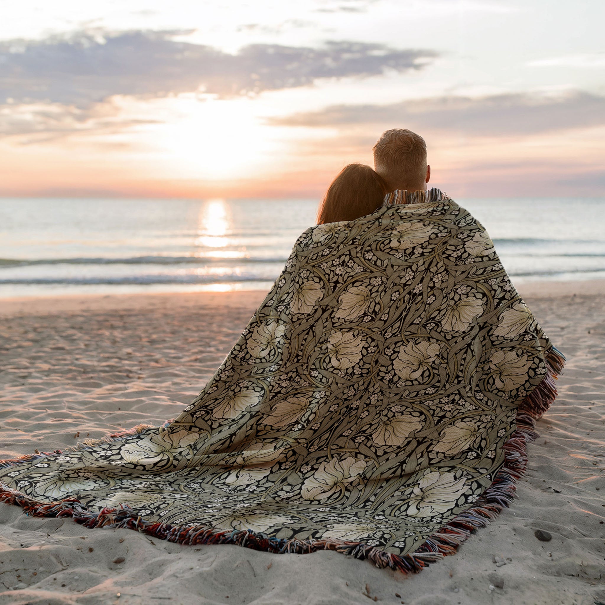 William Morris Pimpernel woven blanket used outdoors at sunset, cozy botanical throw for beach or travel, in sage green and cream on black